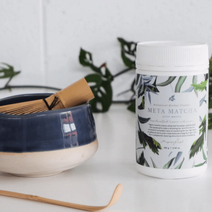 Mayella Meta Matcha on a white bench with a traditional Japanese bamboo scoop spoon and a bamboo whisk sitting inside a blue and white pottery cup.